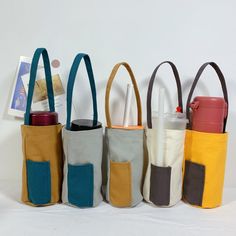 four different colored totes are lined up against a white background, one has a bottle in it and the other is empty