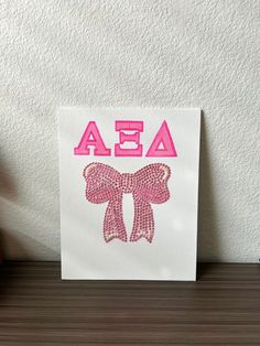 a white card with pink sequins and the word ae on it, sitting next to a red apple