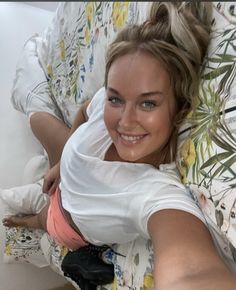 a young woman laying on top of a bed next to a white wall and smiling at the camera