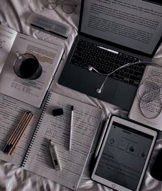 an open laptop computer sitting on top of a bed next to notebooks and pens