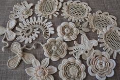 several crocheted flowers and butterflies on a gray surface with white thread in the middle