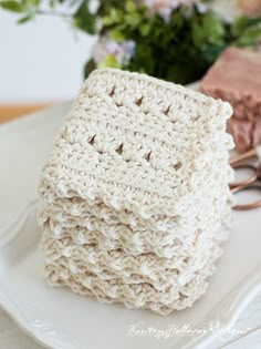 three crocheted napkins sitting on top of a white plate next to flowers