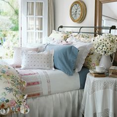 a bed with white sheets and pillows in front of a window next to a clock