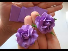 two small purple flowers are being held in someone's hand with an origami object behind them