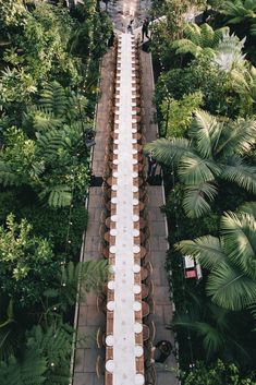 an overhead view of a long table and chairs in the middle of a walkway surrounded by trees