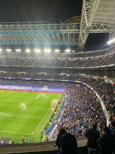 a stadium filled with lots of people watching a soccer game on the field at night