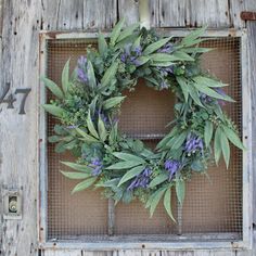 a wreath with purple flowers and green leaves hangs on an old wooden door, surrounded by metal grates