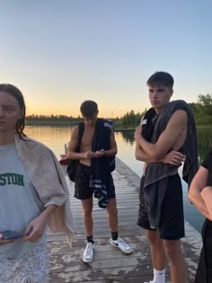 several people standing on a dock by the water at sunset or sunrise, with one person holding a cell phone in his hand