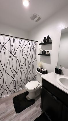 a white toilet sitting next to a bathroom sink under a shower curtain with black lines on it