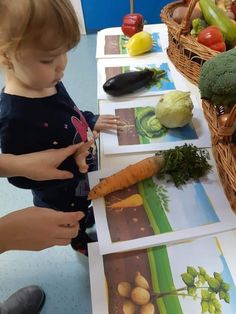 a little boy standing in front of a table with pictures of vegetables and fruits on it