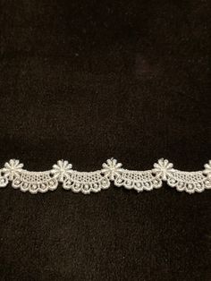 three white lace trims on a black velvet surface, with small flowers in the center