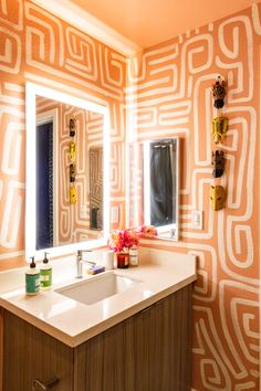 a bathroom with orange and white wallpaper, sink and mirror in front of it