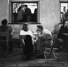 black and white photograph of people sitting at tables in front of a building with windows