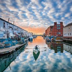 boats are docked in the water near buildings and clouds at sunset on a cloudy day