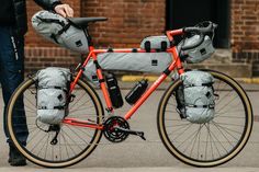 a person standing next to a bike with bags on it's front rack and the rear wheel