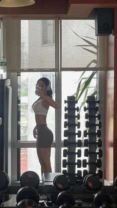 a woman standing in front of a window next to a bunch of dumbbells