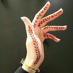 a person's hand painted with red and white baseball stitches on it, holding onto a black surface