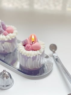 two cupcakes with pink frosting and a lit candle on a silver tray