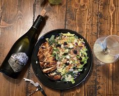 a plate of food next to a bottle of wine and a glass on a wooden table