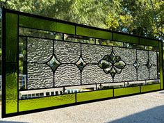 a green stained glass window sitting on the side of a road with trees in the background