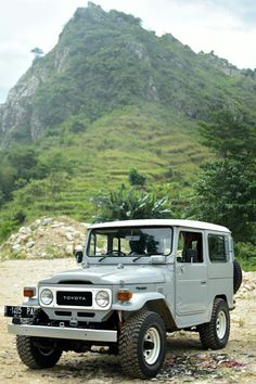 an old jeep is parked in front of a mountain