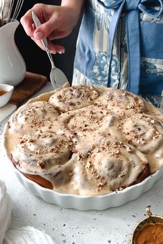 a person is holding a spoon over a dish with cinnamon rolls on it and sauce in the background