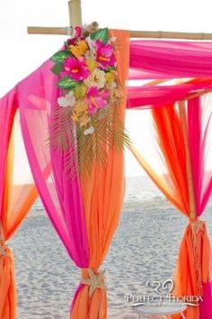 an orange and pink wedding arch with flowers on it at the beach in front of the ocean