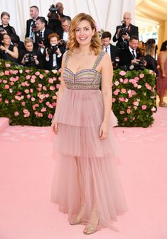 a woman in a long pink dress standing on a pink carpet with cameras around her