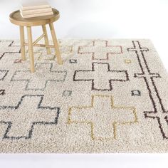 a white rug with an abstract design on the floor and a wooden stool next to it