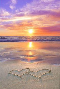 two hearts drawn in the sand on a beach at sunset, with the sun setting behind them