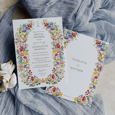 the wedding stationery is laid out on a blue cloth with flowers and leaves around it