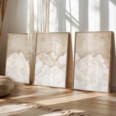 three framed art pieces sitting on top of a hard wood floor next to a window