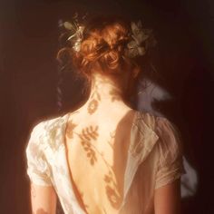 the back of a woman's dress with flowers in her hair and leaves on it