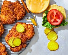 fried chicken with pickles and tomatoes on a cooling rack next to some breaded buns