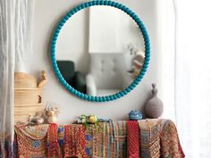 a round mirror hanging on the wall next to a table with pillows and vases