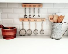 kitchen utensils hanging on the wall in front of pots and measuring spoons