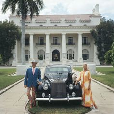 two men standing next to a car in front of a large white building with columns