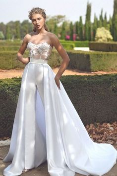 a woman standing in front of a hedge wearing a white dress