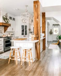 an open concept kitchen and living room with wood flooring, white cabinets and bar stools