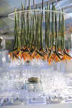 an arrangement of flowers hanging from the ceiling over a table set with wine glasses and place settings