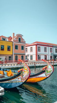 two boats are tied to the dock in front of some buildings and people walking on the pier