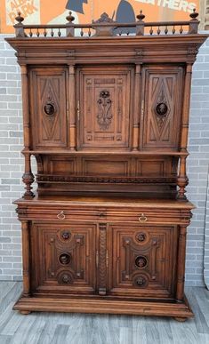 an old wooden cabinet with carvings on the top and bottom, in front of a brick wall