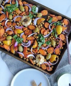 a pan filled with vegetables and beans on top of a table next to silverware