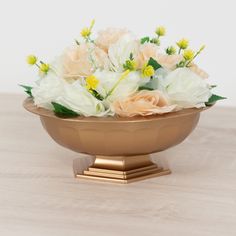 a gold bowl filled with flowers on top of a wooden table