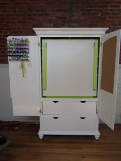 a white cabinet with two drawers and an umbrella hanging on the wall behind it, in front of a brick wall