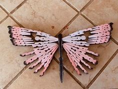 a pink and black butterfly made out of toothpicks sitting on a tile floor