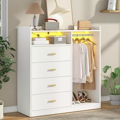 a white cabinet filled with clothes next to a lamp and potted plant on top of a hard wood floor