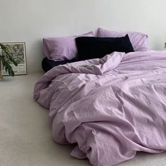 an unmade bed with purple sheets and pillows on the floor next to a potted plant