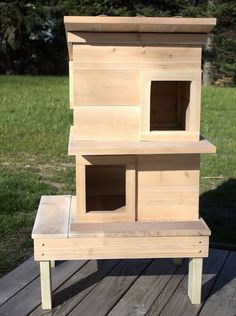 a wooden bird house sitting on top of a wooden deck next to grass and trees