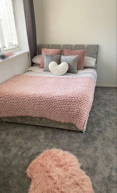 a bed with pink blankets and pillows in a bedroom next to a window on the floor